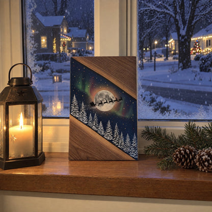 Sleigh and Moon Christmas board on a windowsill beside a candle lantern, snow falling outside